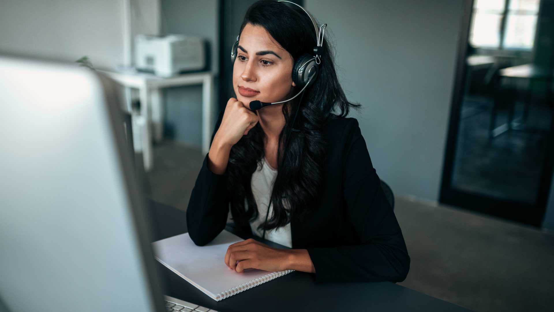 Pensive businesswoman with headset looking at computer screen.